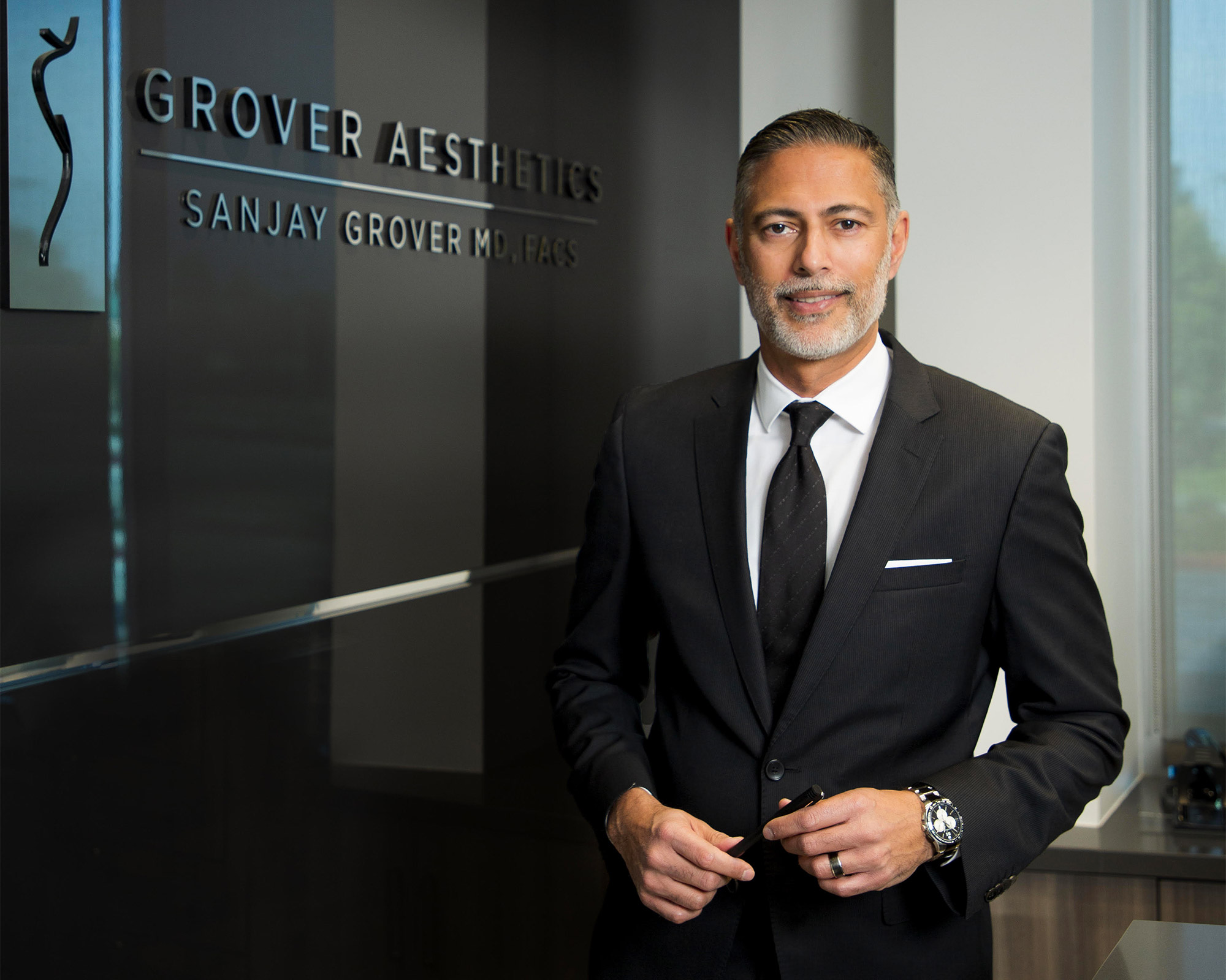 Dr. Grover smiling, wearing a nice black suit, holding a sleek black pen