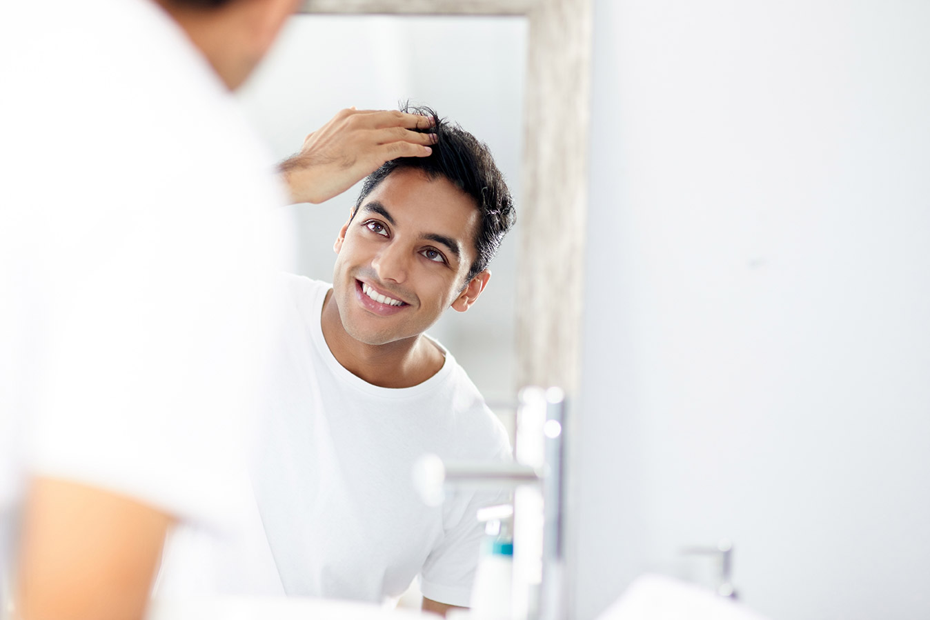 Man smiling, looking into the mirror, running his fingers through his hair